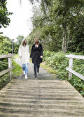 Twee vrouwen wandelen over een houten brug in het groen